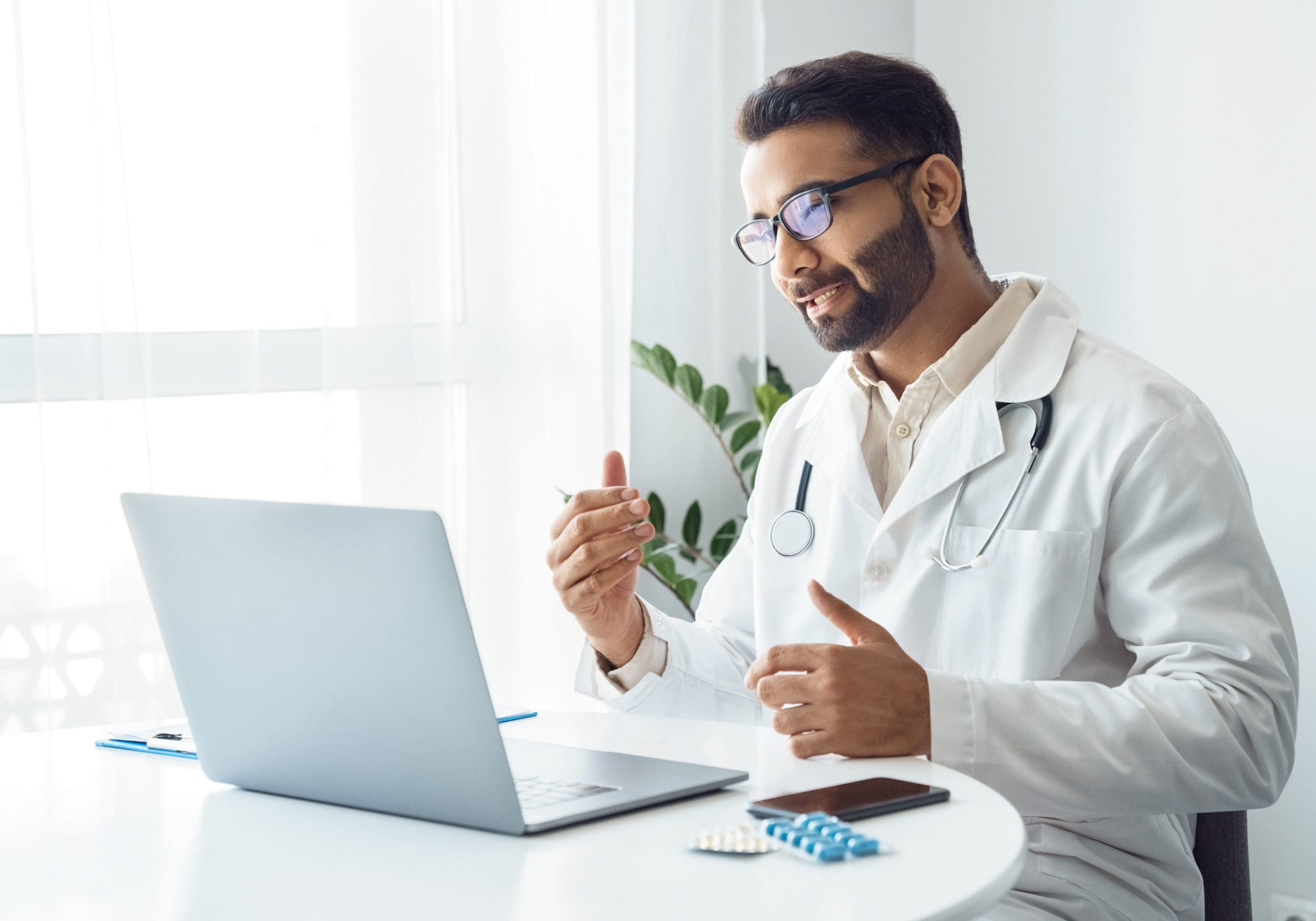 A man in white lab coat sitting at table with laptop.